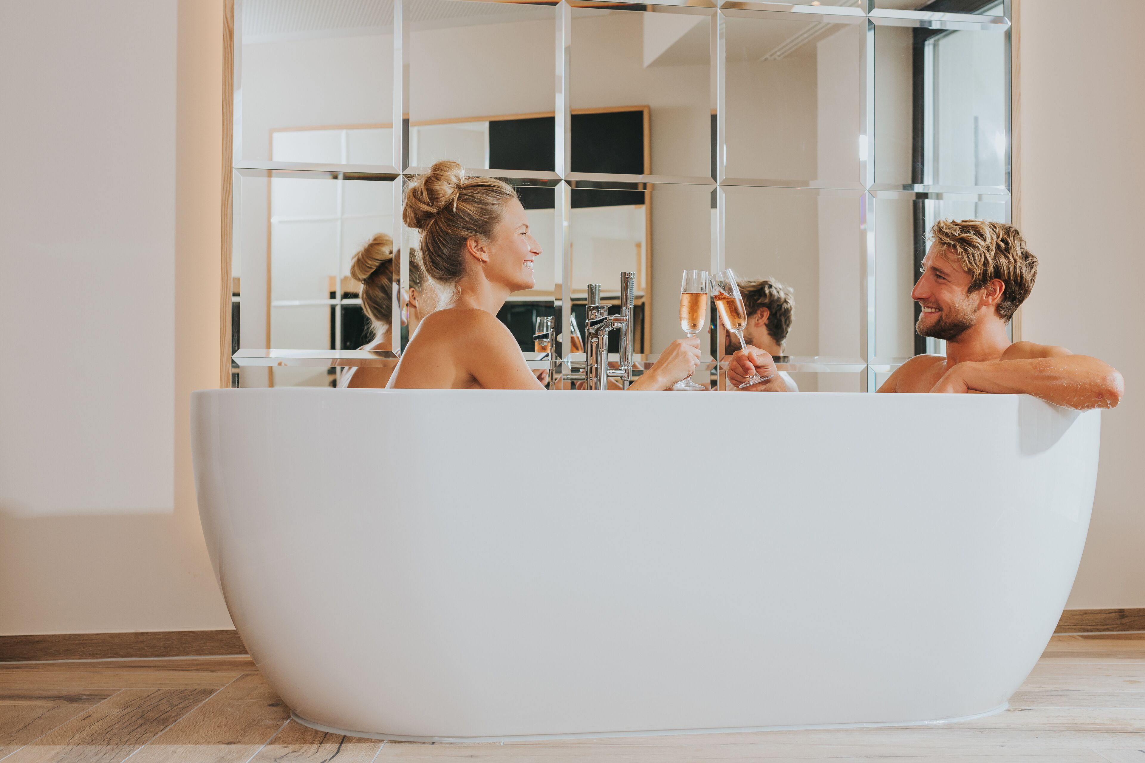 Ein modernes Badezimmer mit einer großzügigen, freistehenden Badewanne, einem großen Spiegel und einem Fenster, das für natürliches Licht sorgt.