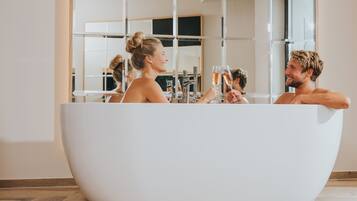 Ein modernes Badezimmer mit einer großzügigen, freistehenden Badewanne, einem großen Spiegel und einem Fenster, das für natürliches Licht sorgt.