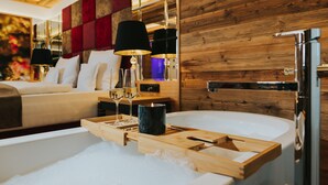 A modern bathroom with a bathtub, wooden tray, and two glasses of wine. - Ortners Resort (Bad Fuessing)