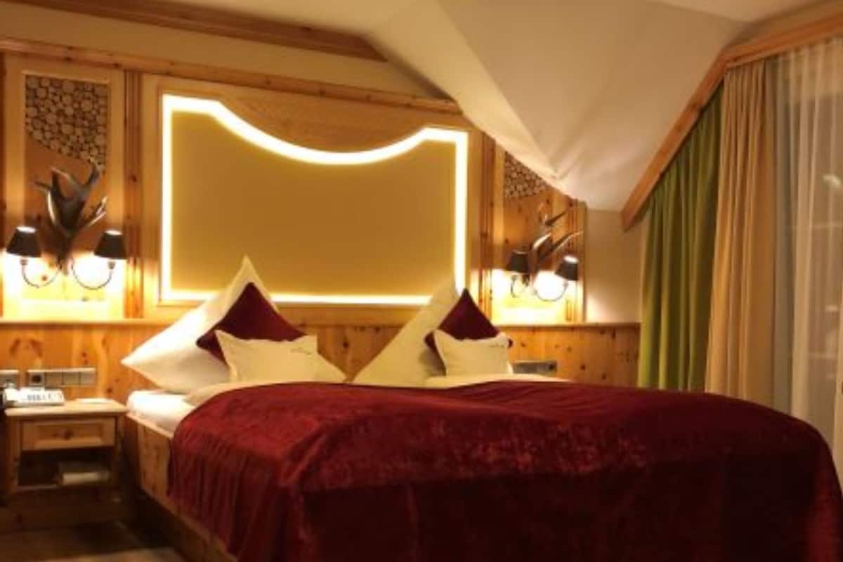 A cozy bedroom with a wooden ceiling, a large bed with a red bedspread, two bedside tables with lamps, and a wall-mounted light fixture.