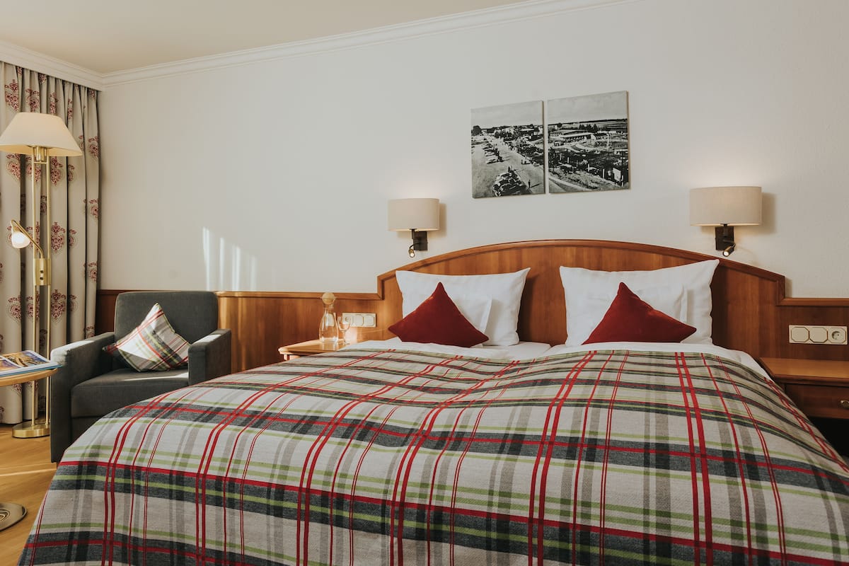 A hotel room with a large bed, two bedside lamps, a nightstand, a chair, and a table with a lamp.