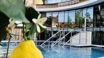 Zona de piscina con un edificio moderno al fondo, un limón amarillo colgando de una rama y un cielo despejado.