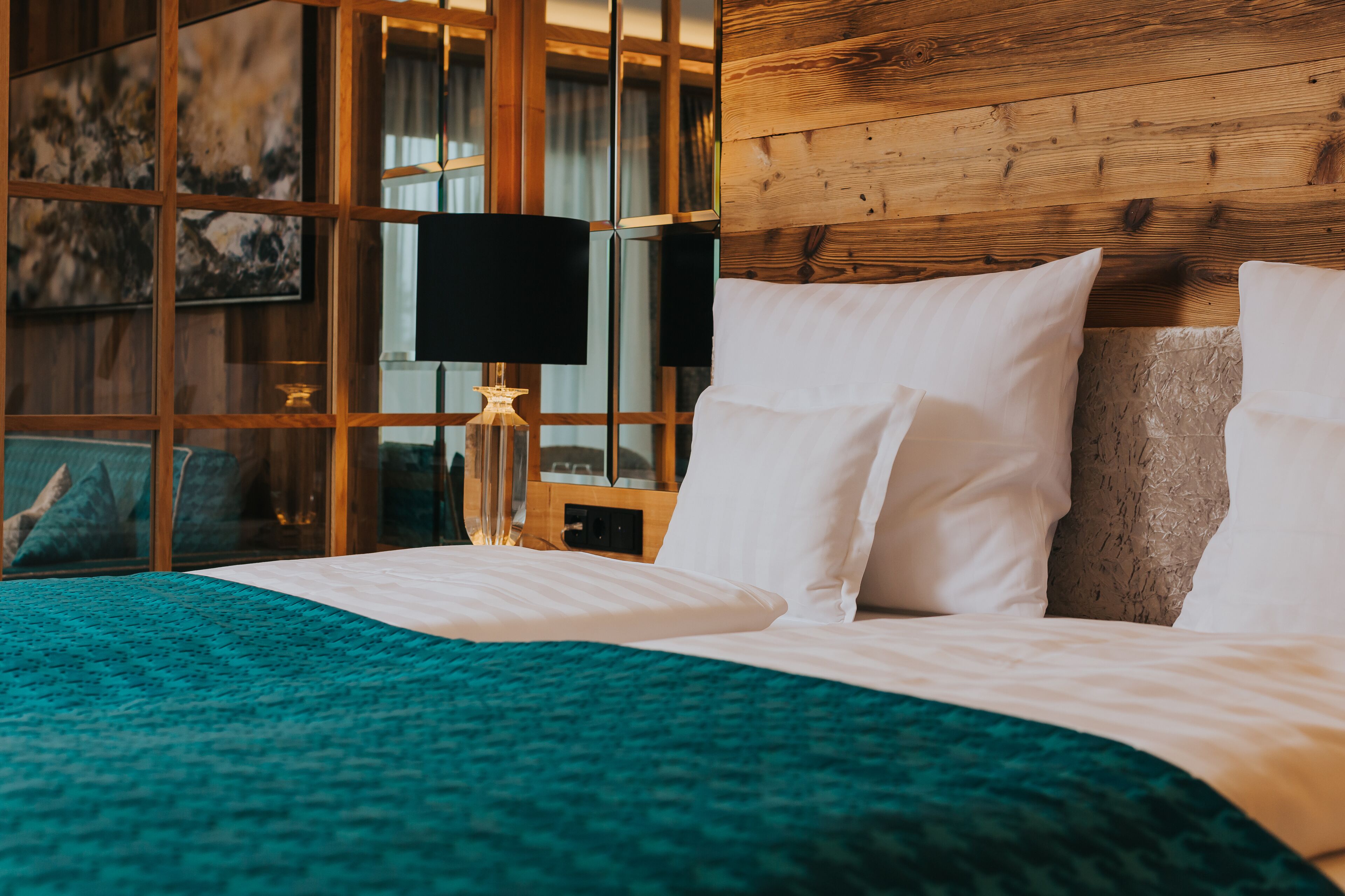 A neatly made bed with white linens, a teal throw blanket, and a wooden headboard.