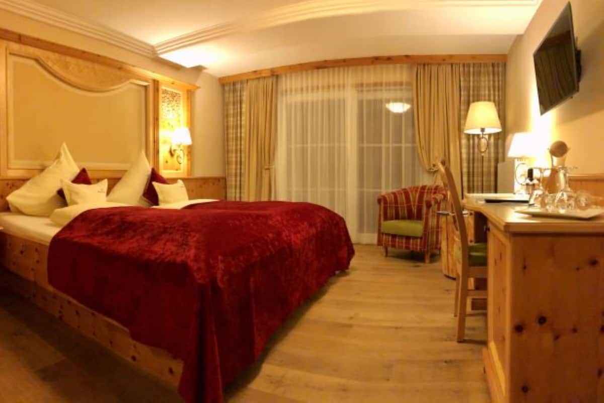 A hotel room with a large bed, a desk, a chair, and a television on the wall.