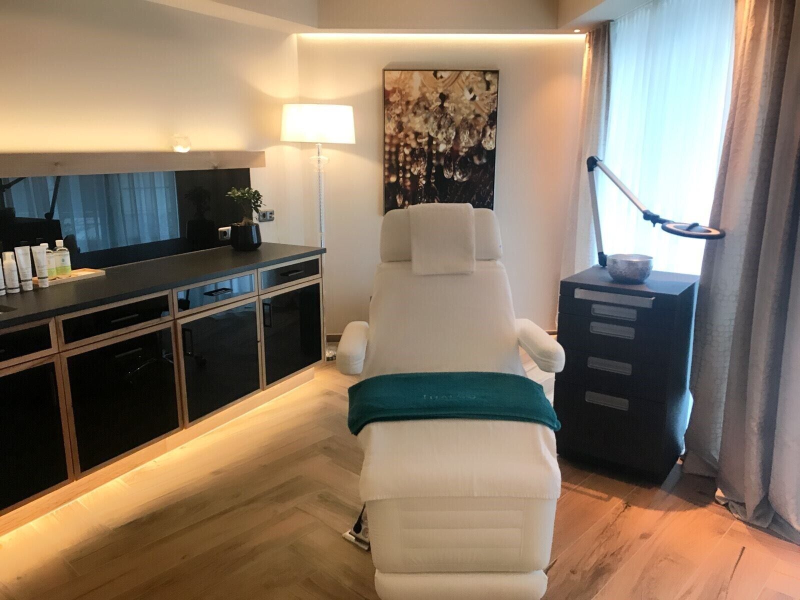 Et moderne værelse med en massagestol, et skrivebord med toiletartikler og et stort abstrakt maleri.