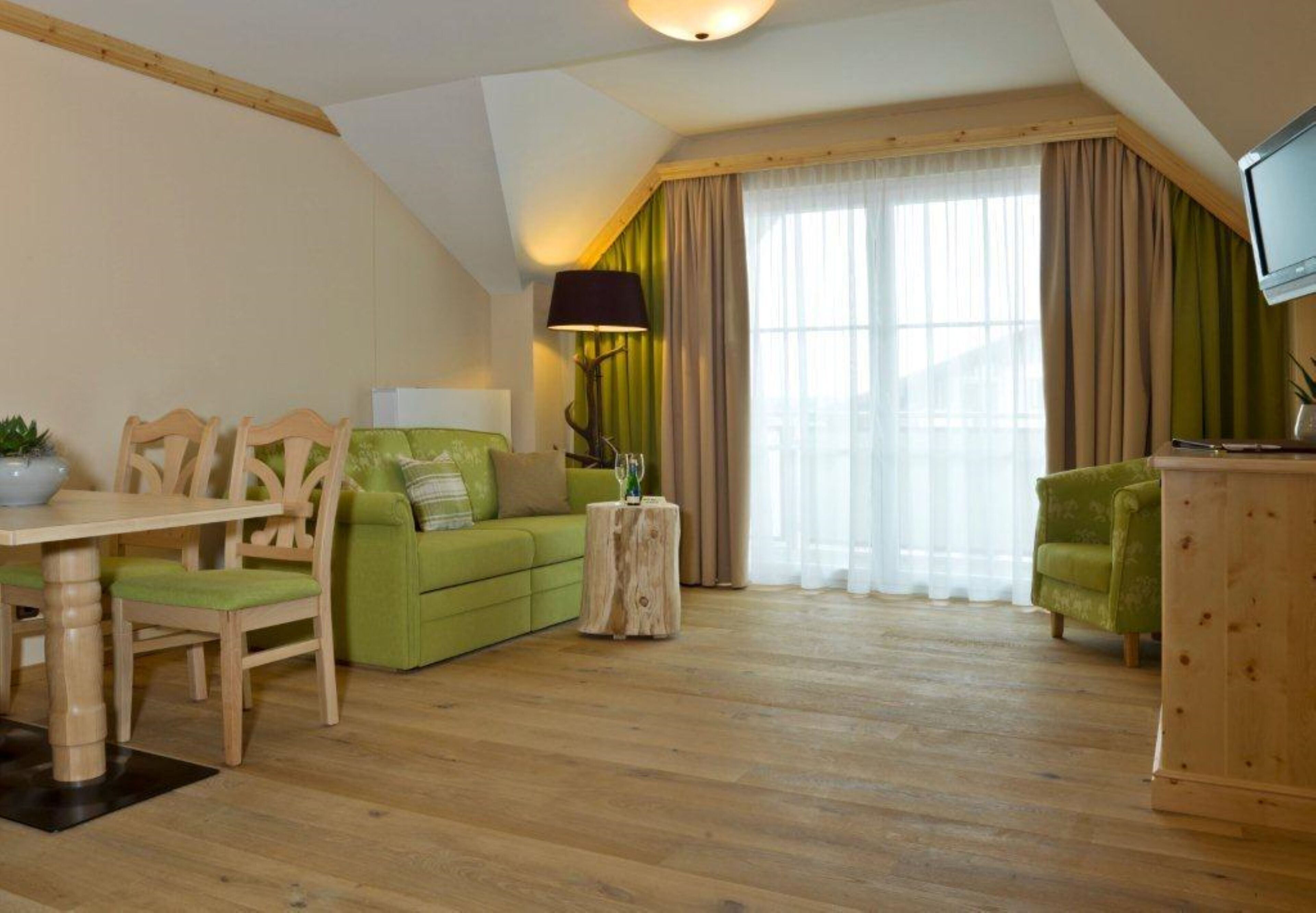 A cozy living room with a wooden dining table, green sofa, and a TV mounted on the wall.
