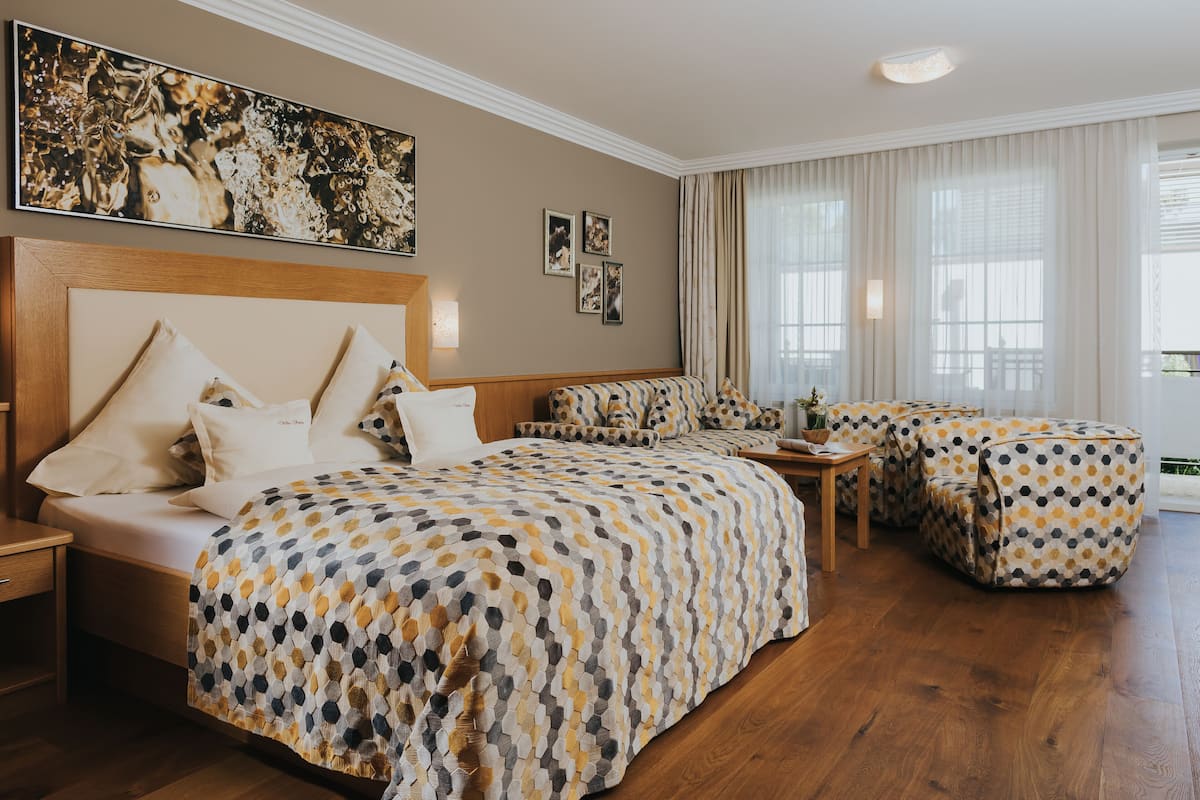A hotel room with a large bed, a sofa, and a small table. There are curtains on the windows and a painting on the wall.
