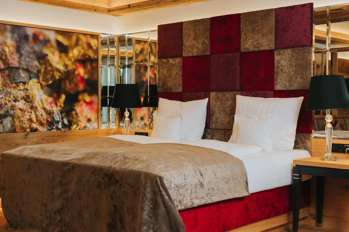 A hotel room with a large bed, a red and brown headboard, and a large abstract painting on the wall.