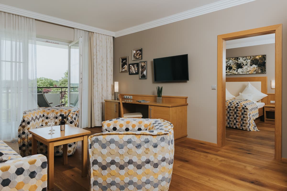 A modern hotel room with a wooden desk, a flat-screen TV, a sofa, and a bed with a patterned bedspread.