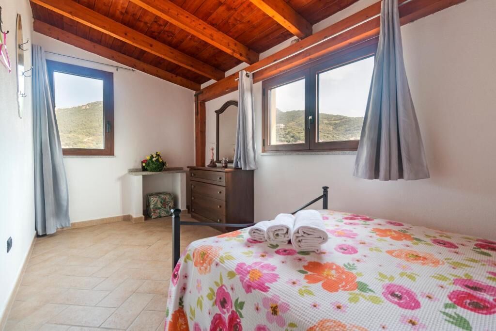 Un dormitorio con cama, cómoda, espejo y dos ventanas con cortinas.
