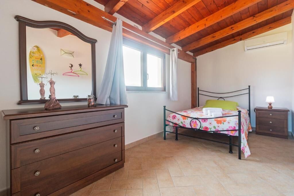 Ein Schlafzimmer mit Holzboden, einem Bett mit floralem Überwurf, einem Schminktisch, einem Nachttisch und einem an der Wand befestigten Spiegel.
