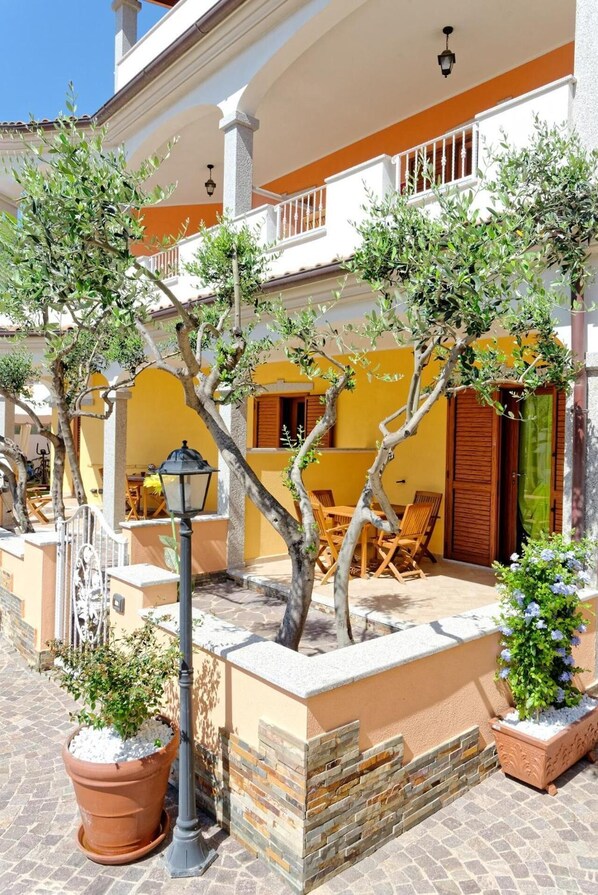 A courtyard with a yellow building, outdoor seating, and potted plants.