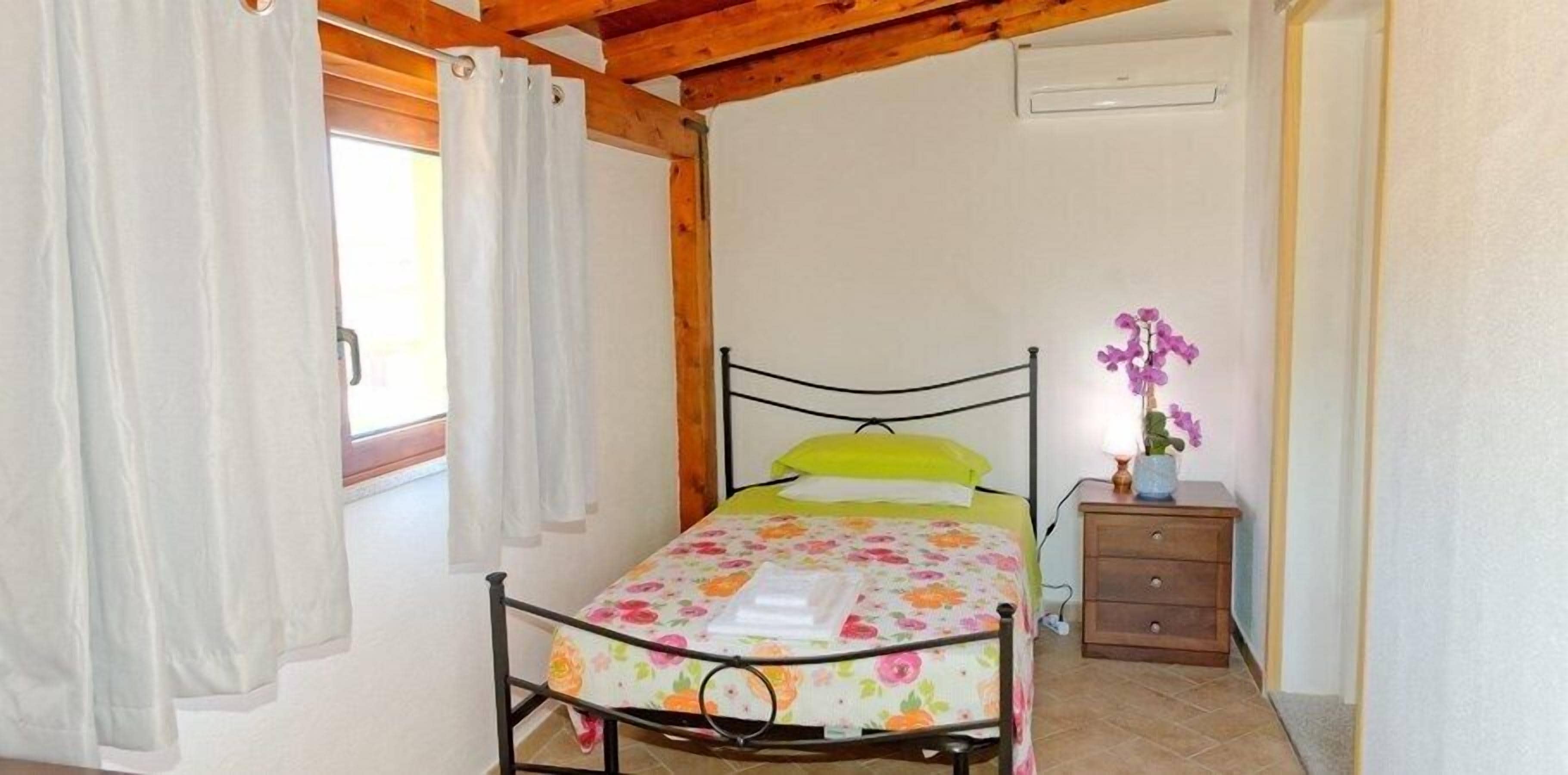 A bedroom with a bed, curtains, a nightstand, and a window.