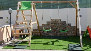 Een houten schommel met een ladder en een stenen muur op de achtergrond.