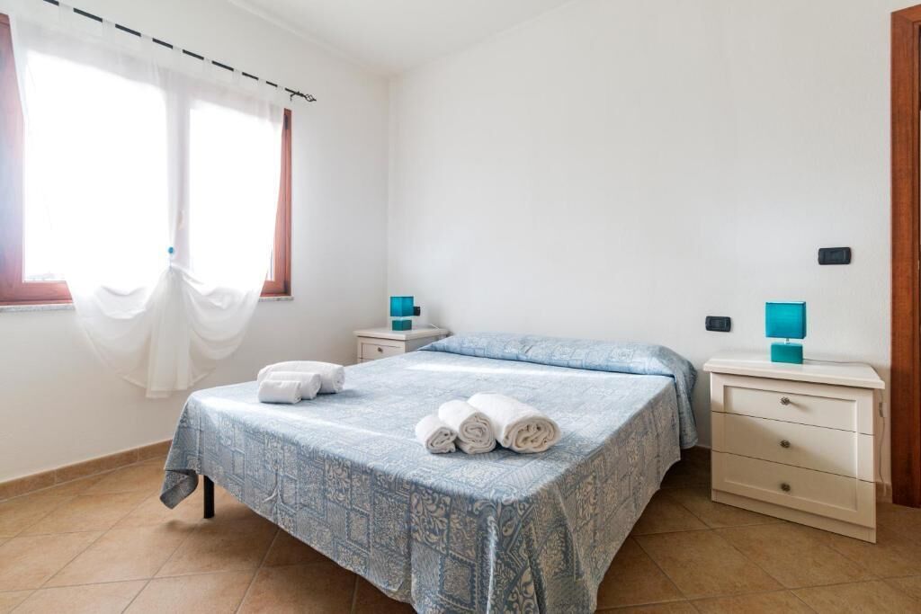 A bedroom with a bed, two bedside tables, a nightstand, and a window with curtains.