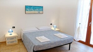 Een slaapkamer met een bed, twee nachtkastjes met lampen, een schilderij aan de muur en uitzicht door een raam.