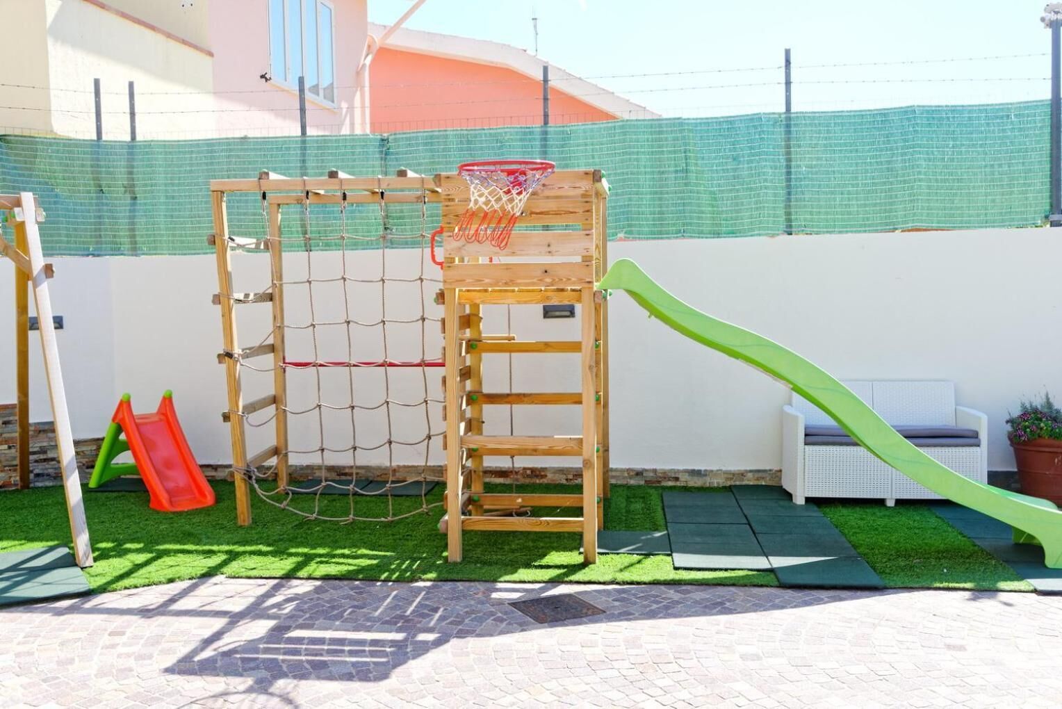 Ein Spielplatz mit einer hölzernen Kletterkonstruktion, einer Rutsche und einem Basketballkorb.