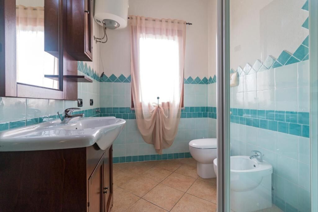 Een badkamer met een wastafel, toilet, bidet en een raam met gordijn.