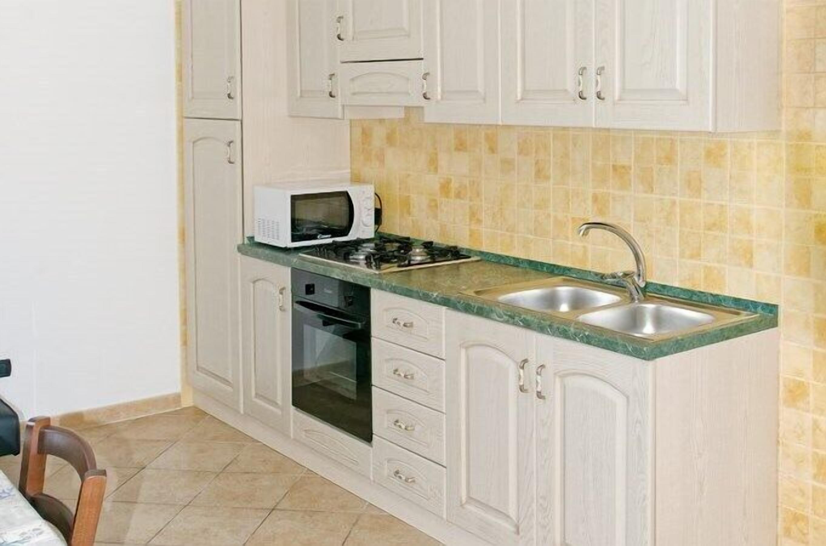 Una cocina con armarios blancos, un microondas, una estufa y un lavamanos.