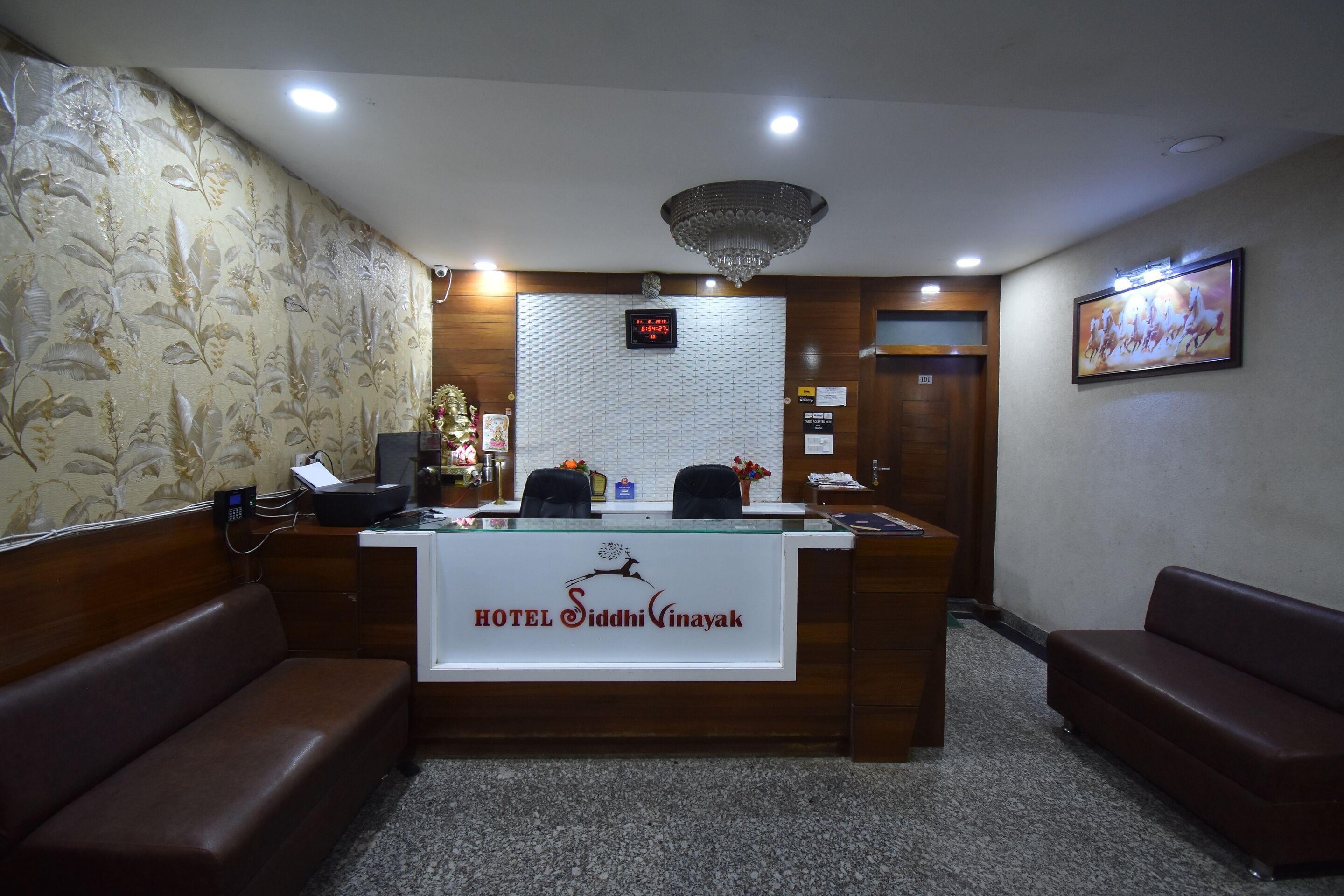 A reception desk with a digital clock, a chandelier, and a framed picture on the wall.