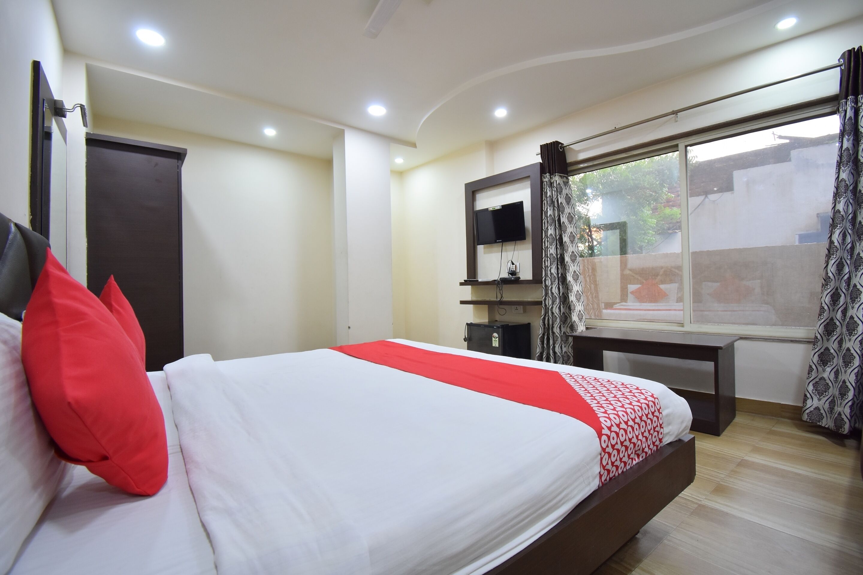 A bedroom with a bed, a desk, a TV, and a window with curtains.
