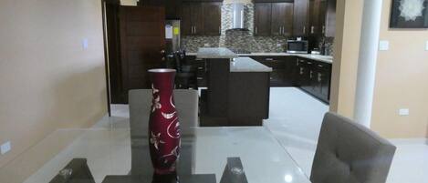 Uma sala de estar moderna com uma mesa de centro de vidro, um vaso vermelho e uma poltrona cinza.
