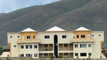 A multi-story building with a central entrance, balconies, and a mountainous backdrop.