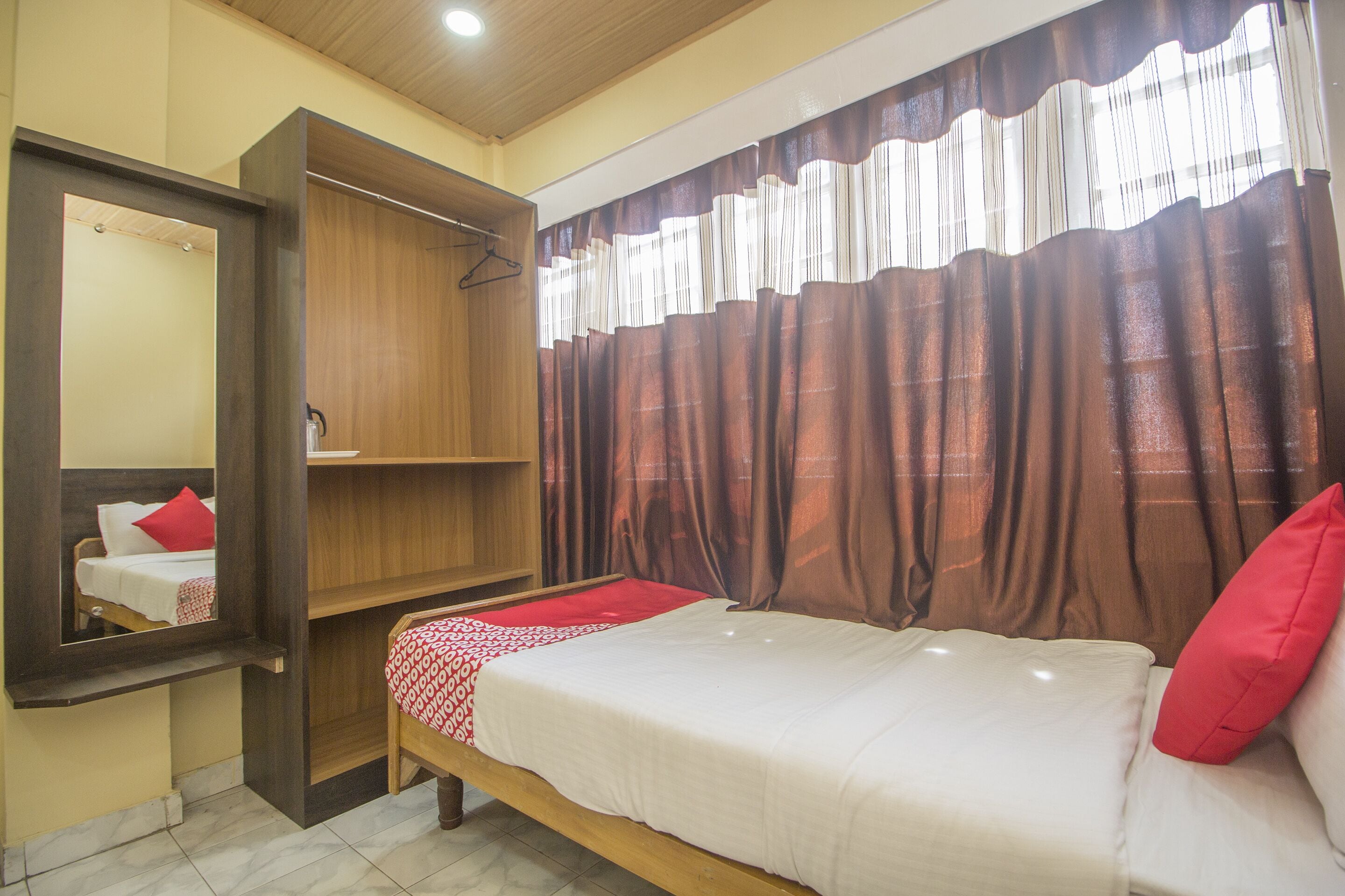 A bedroom with a bed, a mirror, a wardrobe, and a window with curtains.