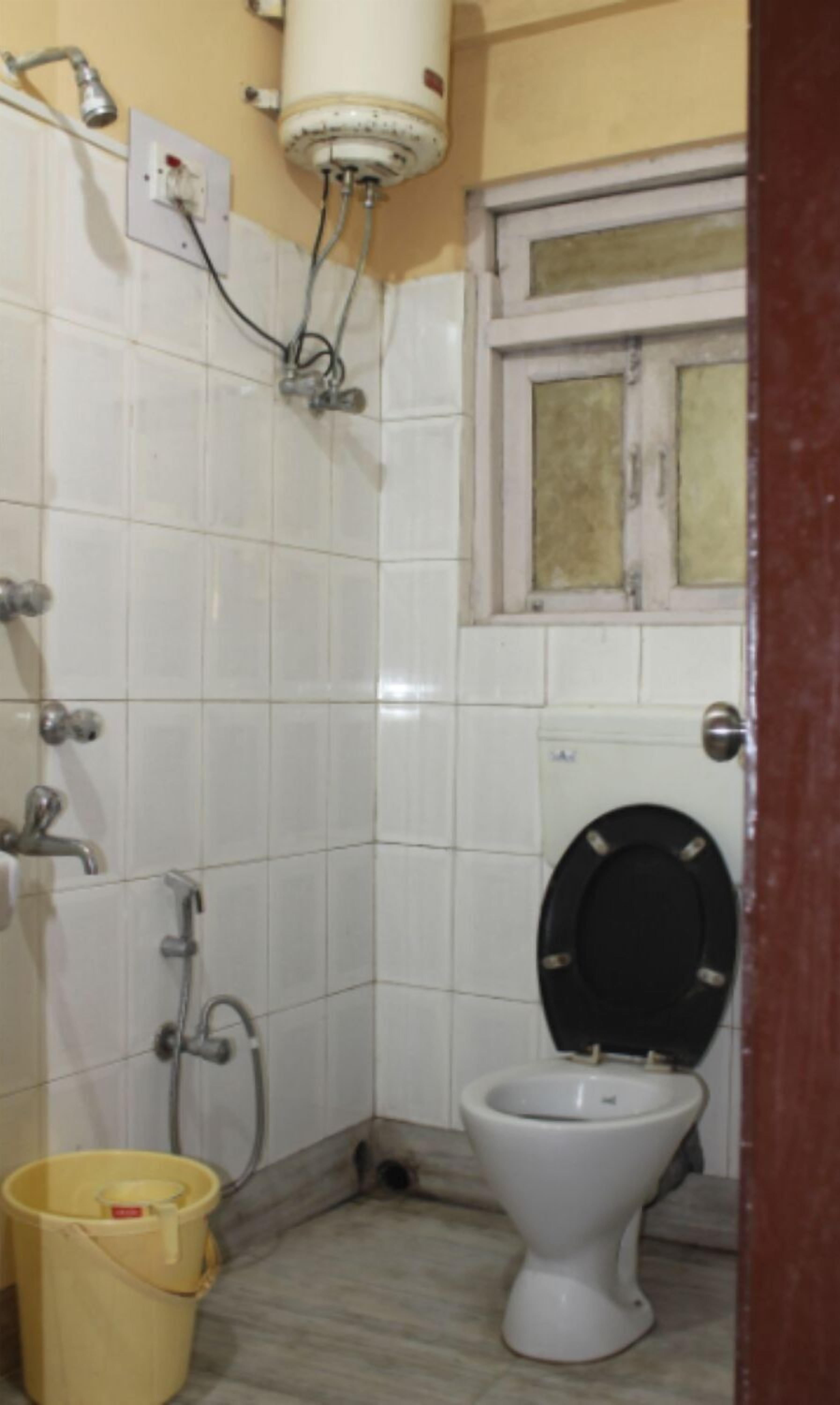 A small bathroom with a toilet, a shower, and a water heater mounted on the wall.