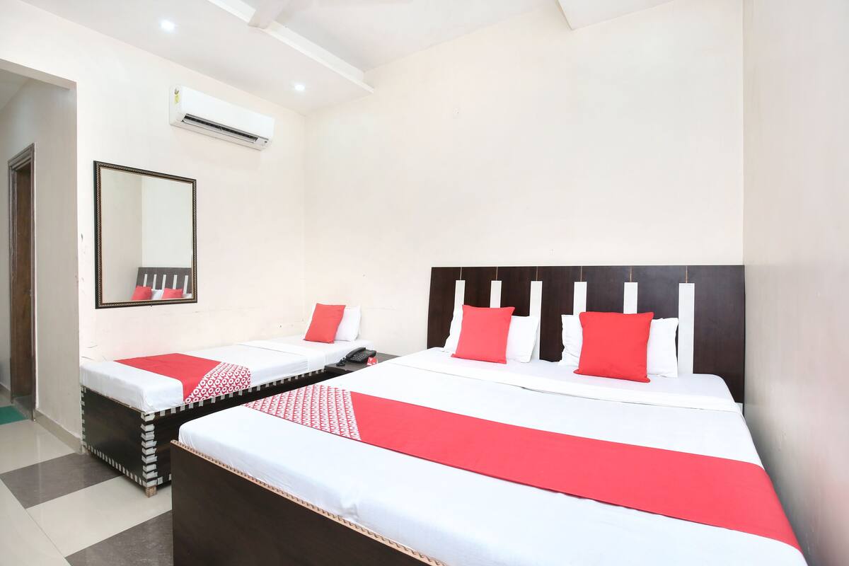 A hotel room with two beds, each with a red and white bedspread, a large mirror, and an air conditioning unit on the wall.