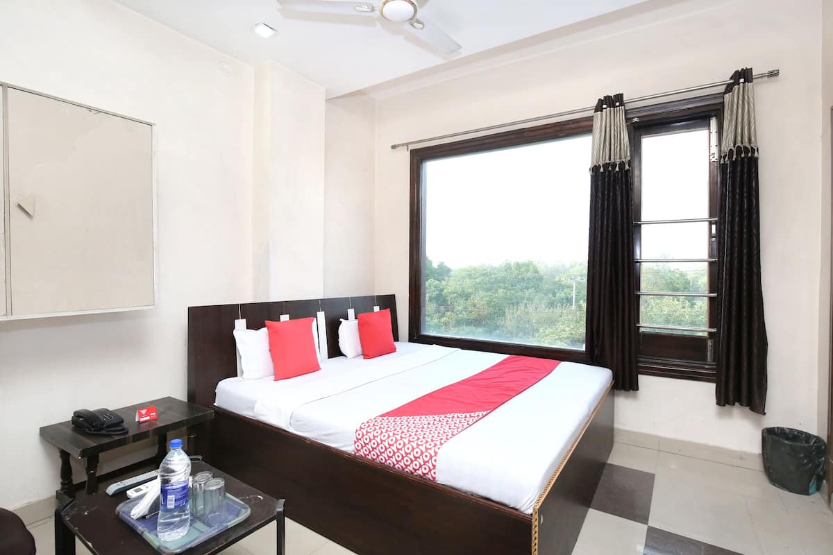 A hotel room with a bed, a window with curtains, a desk with a phone, a trash bin, and a ceiling fan.