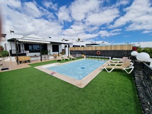 Ein Swimmingpool mit Kunstrasen, Liegestühlen und einer überdachten Sitzgruppe.