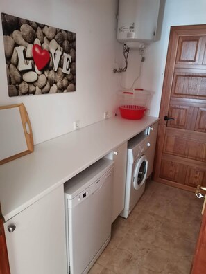 Eine kleine Küche mit Waschmaschine, Wäscheständer und Holztür.