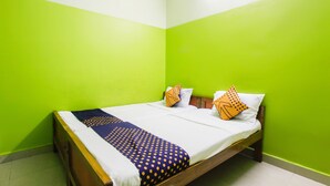Un lit simple avec une couvre-lit à pois bleus et jaunes, deux oreillers à motifs orange et noirs, et une tête de lit en bois, dans une pièce aux murs verts.
