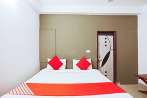 A neatly made bed with white and red bedding, a wooden door with a handle, and a small table with a chair.
