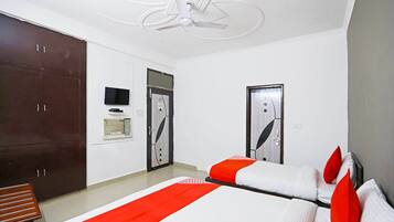 A hotel room with two beds, a wardrobe, a television, and a ceiling fan.