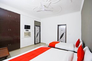Une chambre d’hôtel avec deux lits, une armoire, un téléviseur et un ventilateur de plafond.