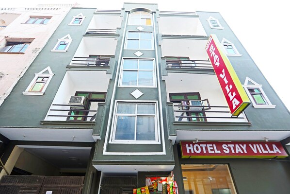 Un immeuble à plusieurs étages avec une enseigne indiquant « HÔTEL STAY VILLA » et une banderole rouge avec du texte blanc.