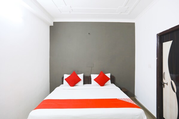 A small, single-bed room with a grey wall, white ceiling, and a wooden door.