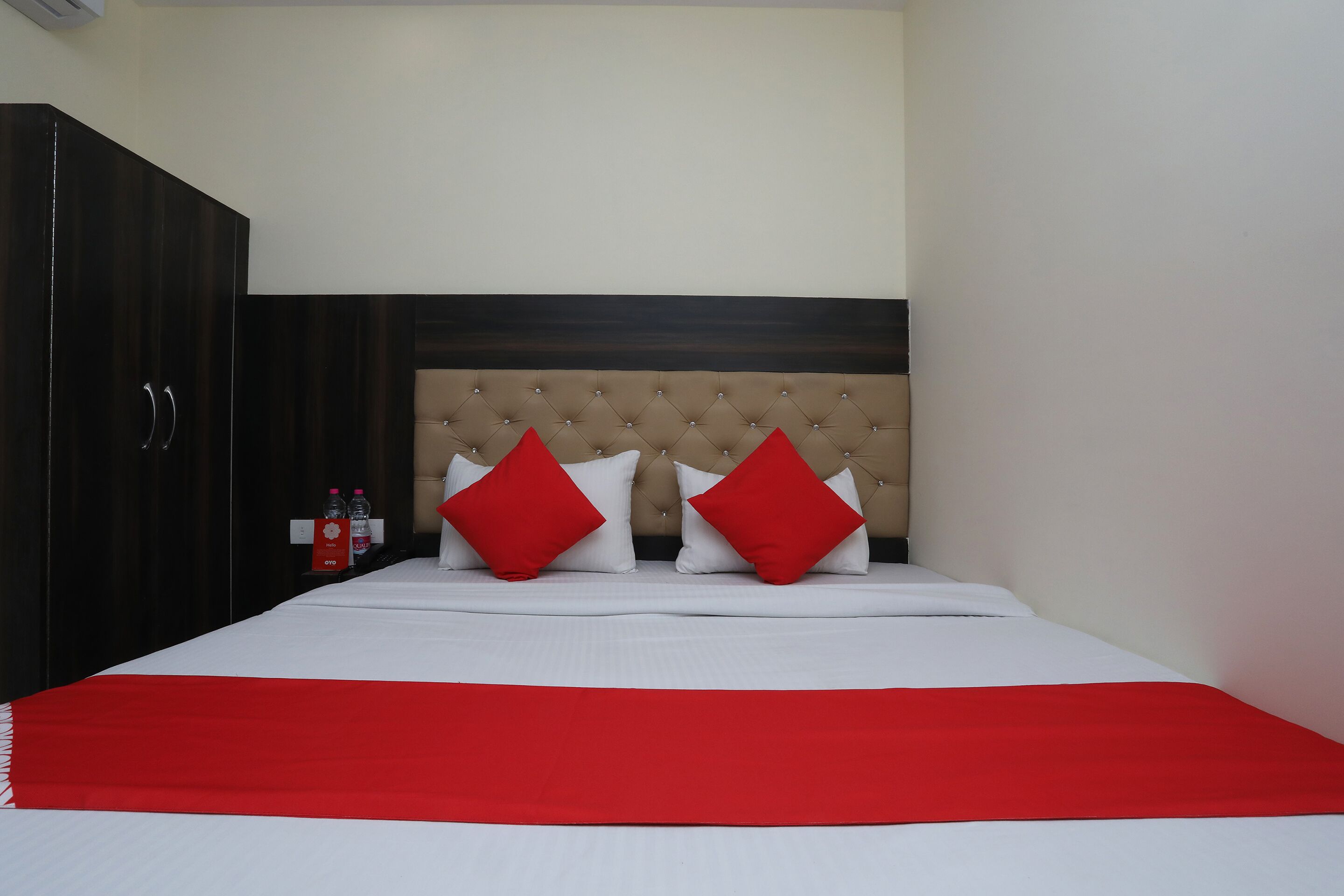 Una habitación de hotel con una cama grande, un armario de madera oscura y un cabecero tapizado en beige.