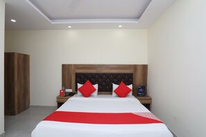A hotel room with a large bed, a wooden headboard, and two red pillows. - OYO 30462 Hotel Ivy (New Delhi)