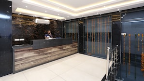 A modern reception area with a marble wall, a wooden reception desk, and a glass door with vertical lines. - OYO 30462 Hotel Ivy (New Delhi)