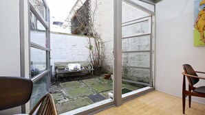 Una habitación con puerta de vidrio corredera que da a un jardín con banco y plantas en macetas.