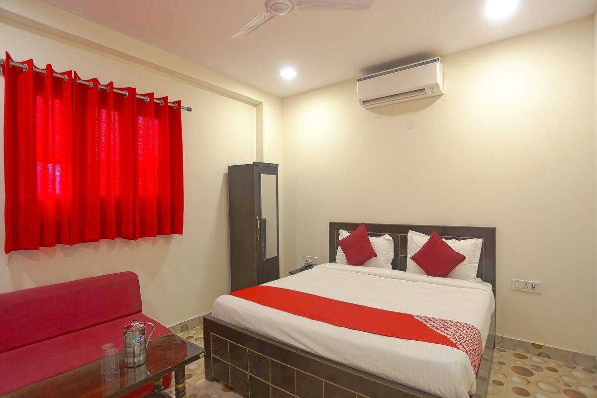 A hotel room with a bed, a red sofa, a small table with a drink, and a ceiling fan.