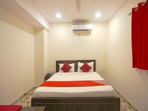 A hotel room with a bed, a nightstand, an air conditioner, and a red curtain. - OYO 41215 Three Kings (New Delhi)