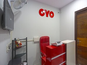 A room with a red chair, a small desk with a printer, a wall-mounted fan, and a sign with the letters "CYO". - OYO 41215 Three Kings (New Delhi)