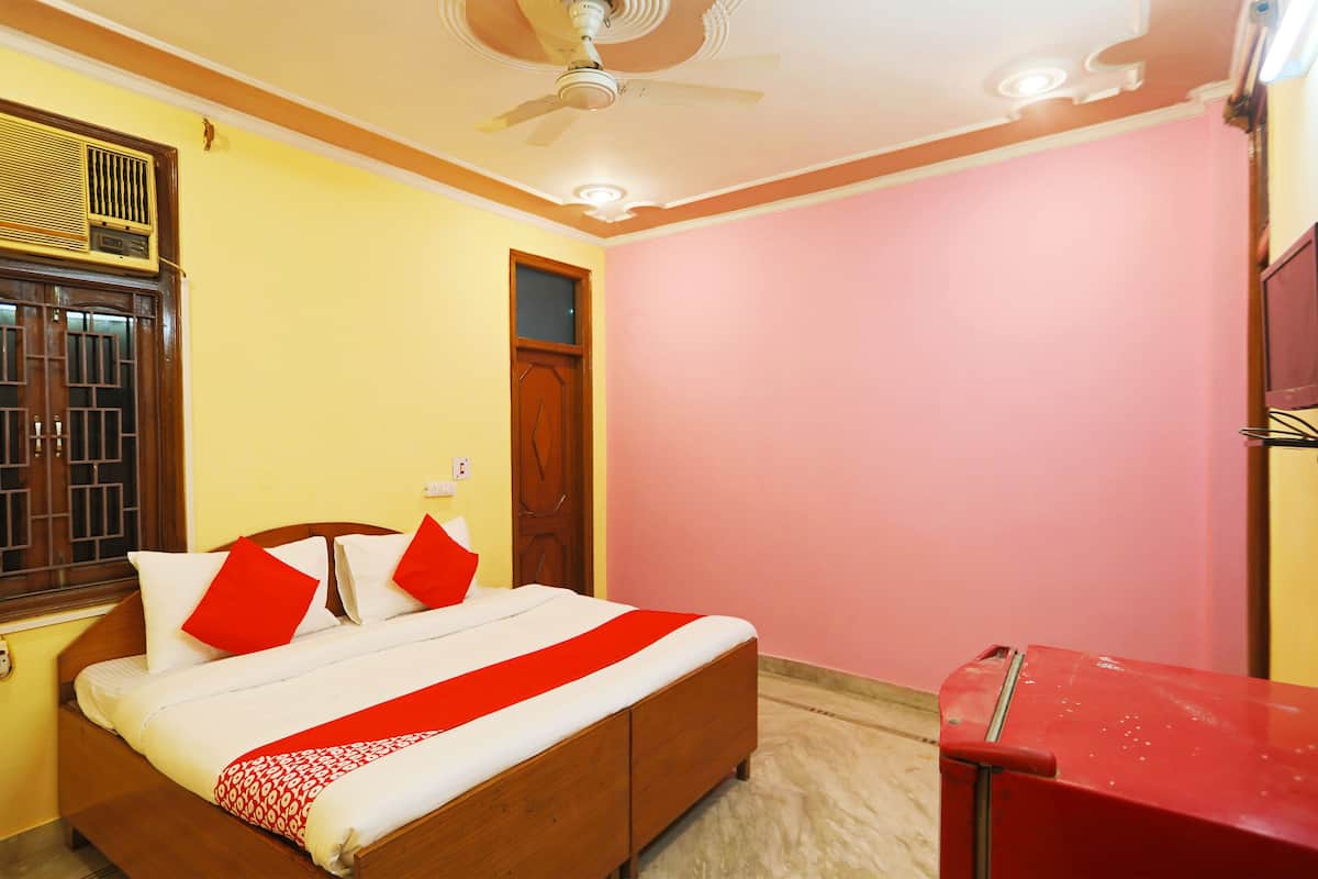 Une pièce avec un lit, un ventilateur de plafond, une fenêtre avec des barreaux et une table rouge.