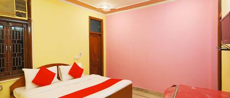 Una habitación con cama, ventilador de techo, ventana con rejas y una mesa roja.