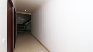 Ein schmaler Flur mit einer Treppe am Ende, weißen Wänden und einem Fliesenboden.