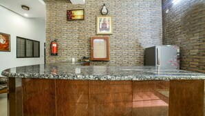A kitchen with a granite countertop, a refrigerator, a fire extinguisher, and a wall-mounted light fixture.